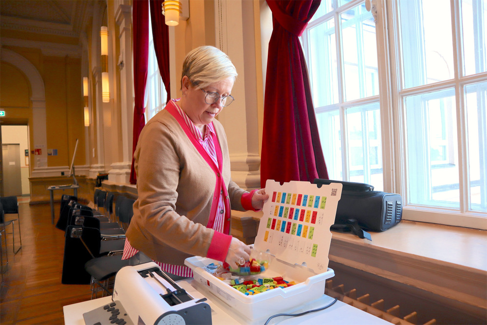 På bilden syns en medelålders kvinna vid namn Misa Möller. Hon har kortklippt blont hår , en rosa och vitrandig skjortblus och en beige tröja med en rad i rosa längs kanten. I bakgrunden ser man höga vitmålade fönster som omges av röda sammetsgardine. Man ser också en vägg i gult och vitt. Kvinnan står halv vänd mot kameran och sorterar något i en låda med legobitar i granna färger. Lådan står på ett bord.