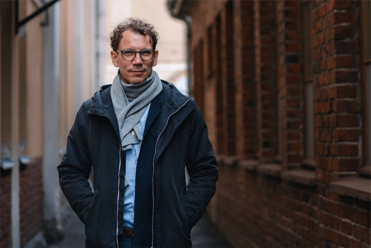 På bilden syns en medelålders man vid namn Juha Itkonen. Han är fotograferad utomhus, han står framför en vägg  i rostbrunt och mörkblått till höger i bilden och till vänster en ljusare nyans. Han är klädd i en mörkblå jacka som är uppknäppt och runt halsen har han en ljusgrå halsduk. Han har brunt lockigt hår och glasögon. Han ser rakt in i kameran och ser allvarlig ut.