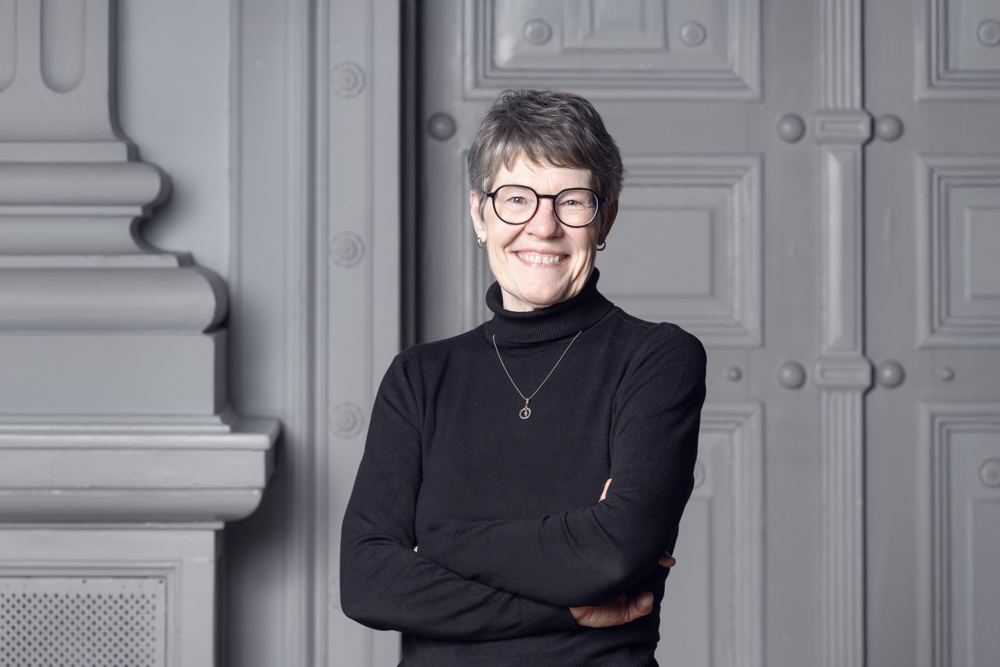 På bilden syns en äldre kvinna vid namn Katarina Rejman. Hon arbetar med utbildningsfrågor på Svenska folkskolans vänner. Hon har kortklippt hår som är både mörkt och grått, hon har mörkbågade glasögon, ser rakt in i kameran och småler. Hon är klädd i svart polotröja och har ett silversmycke runt halsen. I bakgrunden syns vita pelare och spegeldörrar.