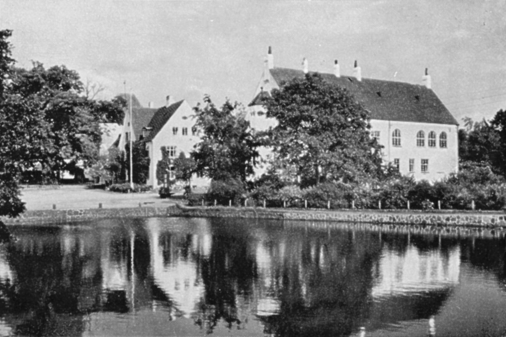 Bilden är en gammal historisk bild i svartvitt som visar ett hus vid en åstrand.