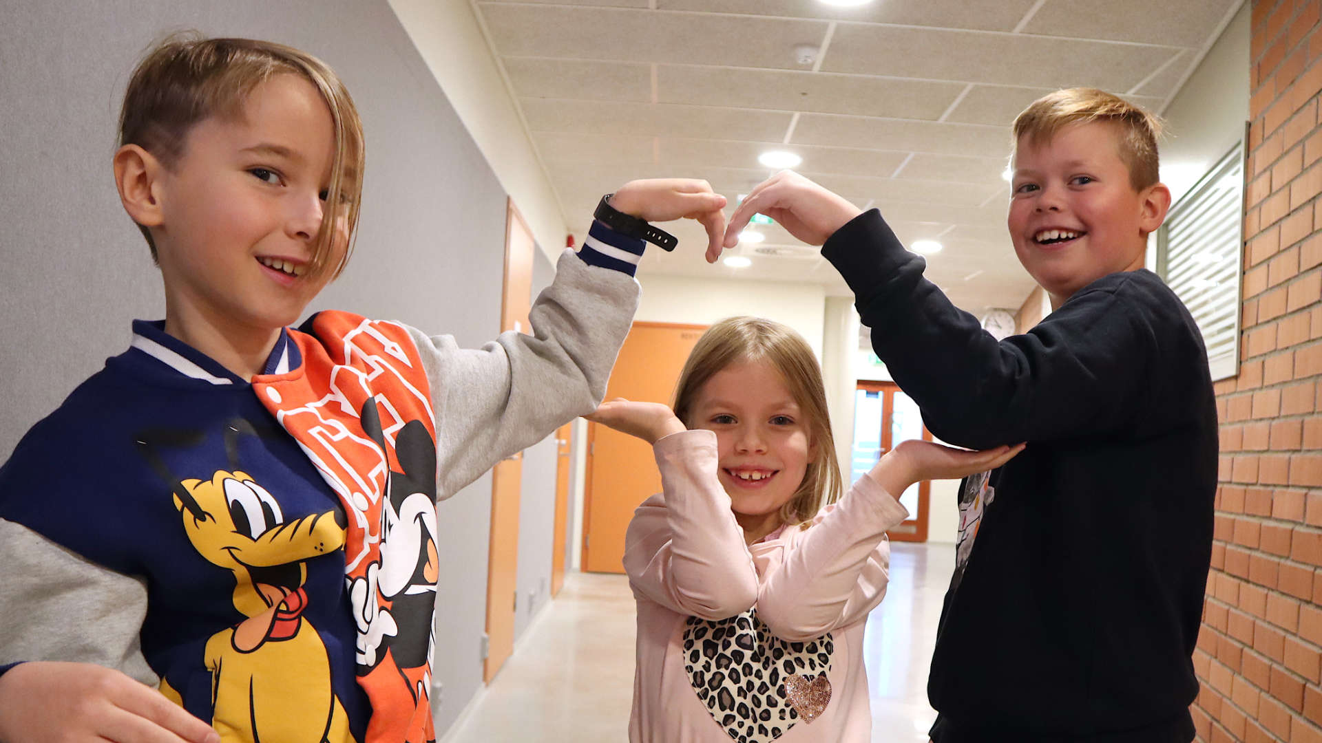 Erik Emaus, Ylva Nyman och Axel Nygård i skolkorrideoren. Med händerna bygger alla tre ett hjärta.